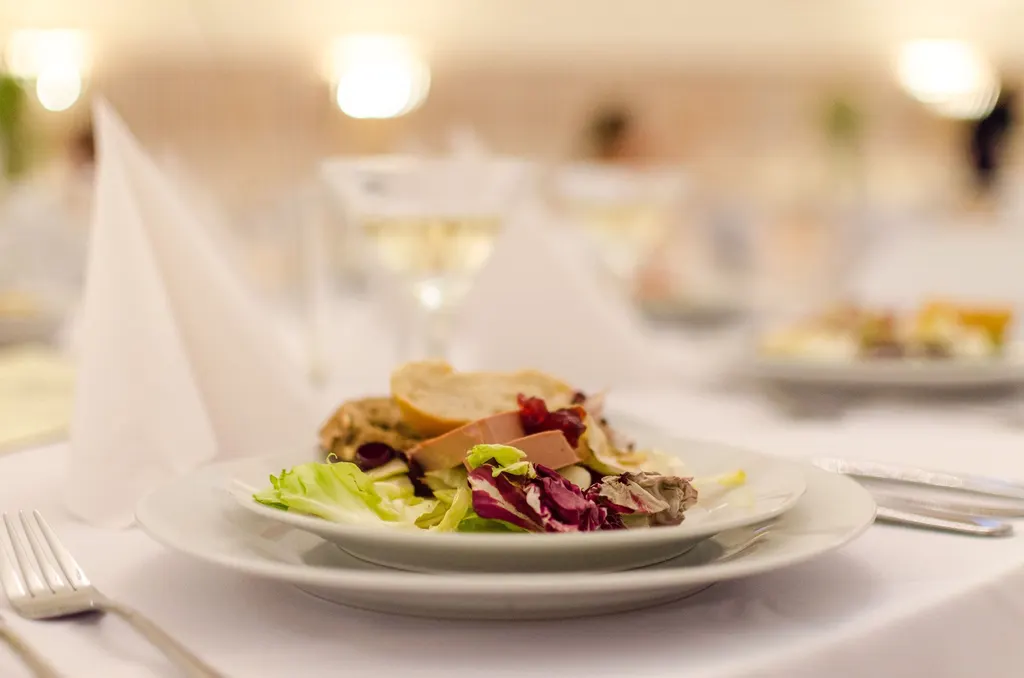 An elegant plated dish on a white-linen table with a glass of wine in a warmly lit restaurant.