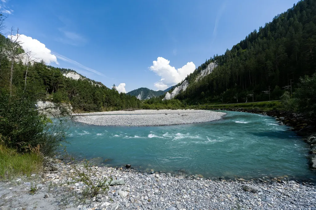 A turquoise mountain river winding through a green forested valley on a clear summer day.
