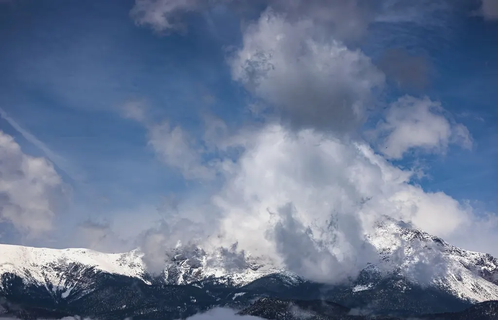 Snow-capped Colorado mountain peaks rising into billowing clouds under a blue winter sky.