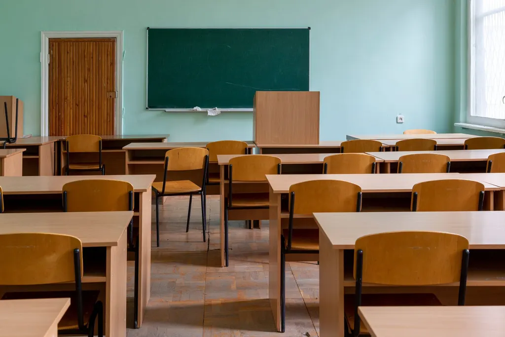 Empty classroom with wooden desks and chairs, a green chalkboard and a large window