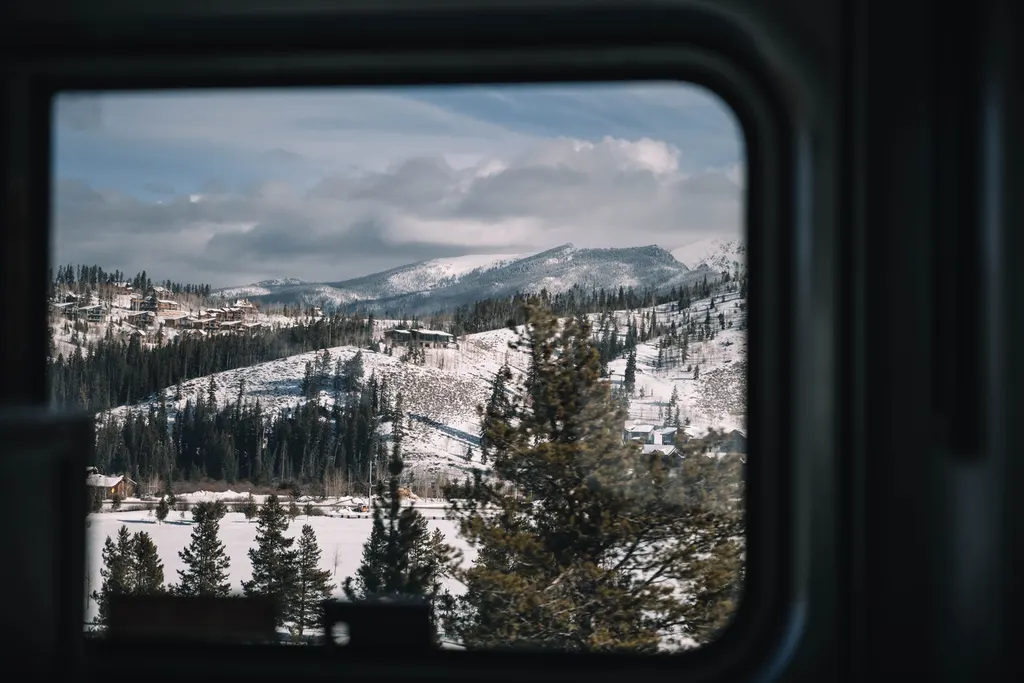 A view through a window of a snowy Colorado mountain town, with homes dotting forested hillsides below snow-capped peaks.