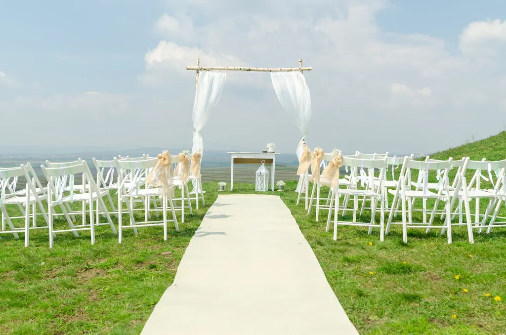 An outdoor wedding ceremony with white chairs and a draped arch on a grassy hillside overlooking the valley.