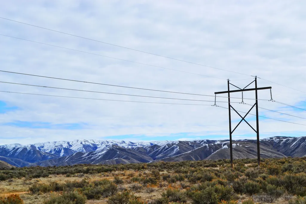 Transmission tower and power lines crossing open sagebrush land toward snow-dusted mountains